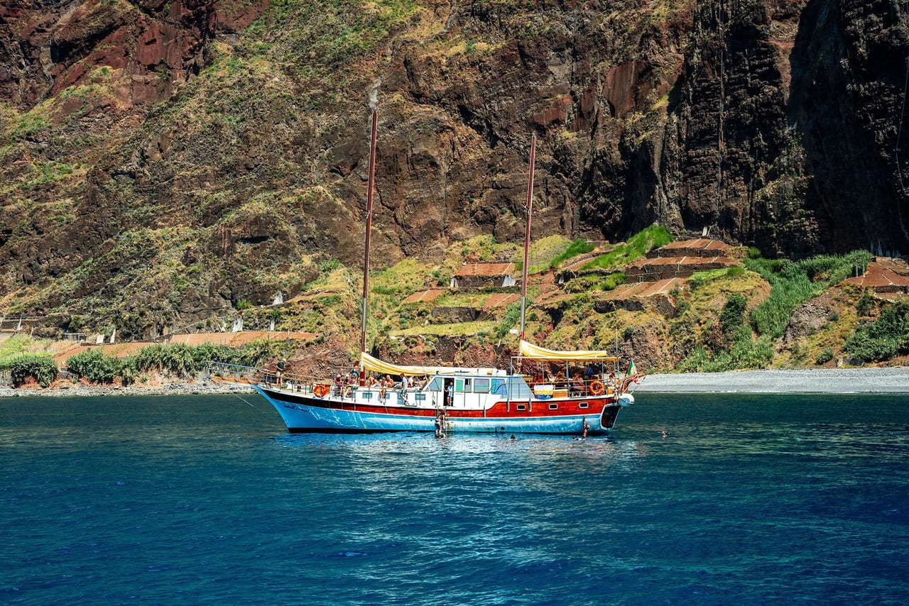 A small boat in a turquoise cove below steep green cliffs
