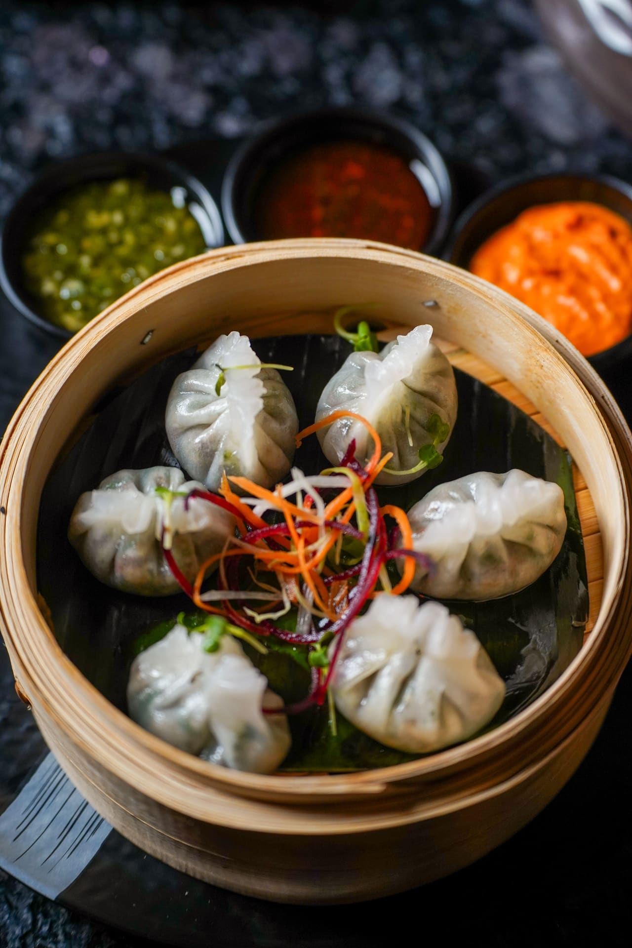 Steamed dim sum in a bamboo basket with small bowls of dipping sauce.