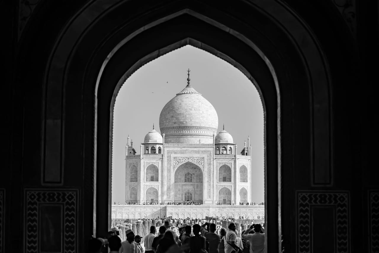 The Taj Mahal framed by a dark arched gateway, in black and white