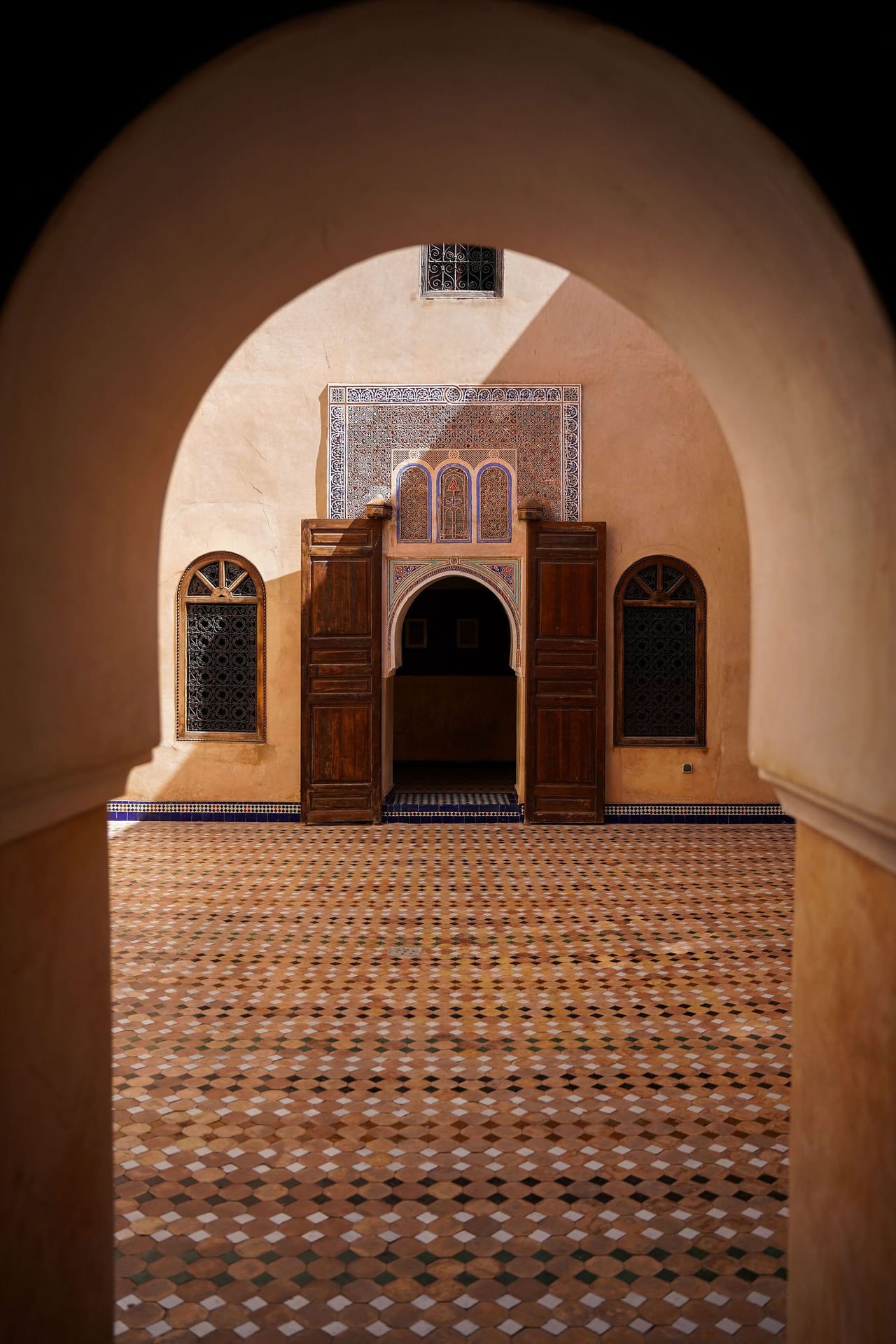 A tiled courtyard and carved doors seen through a pointed arch