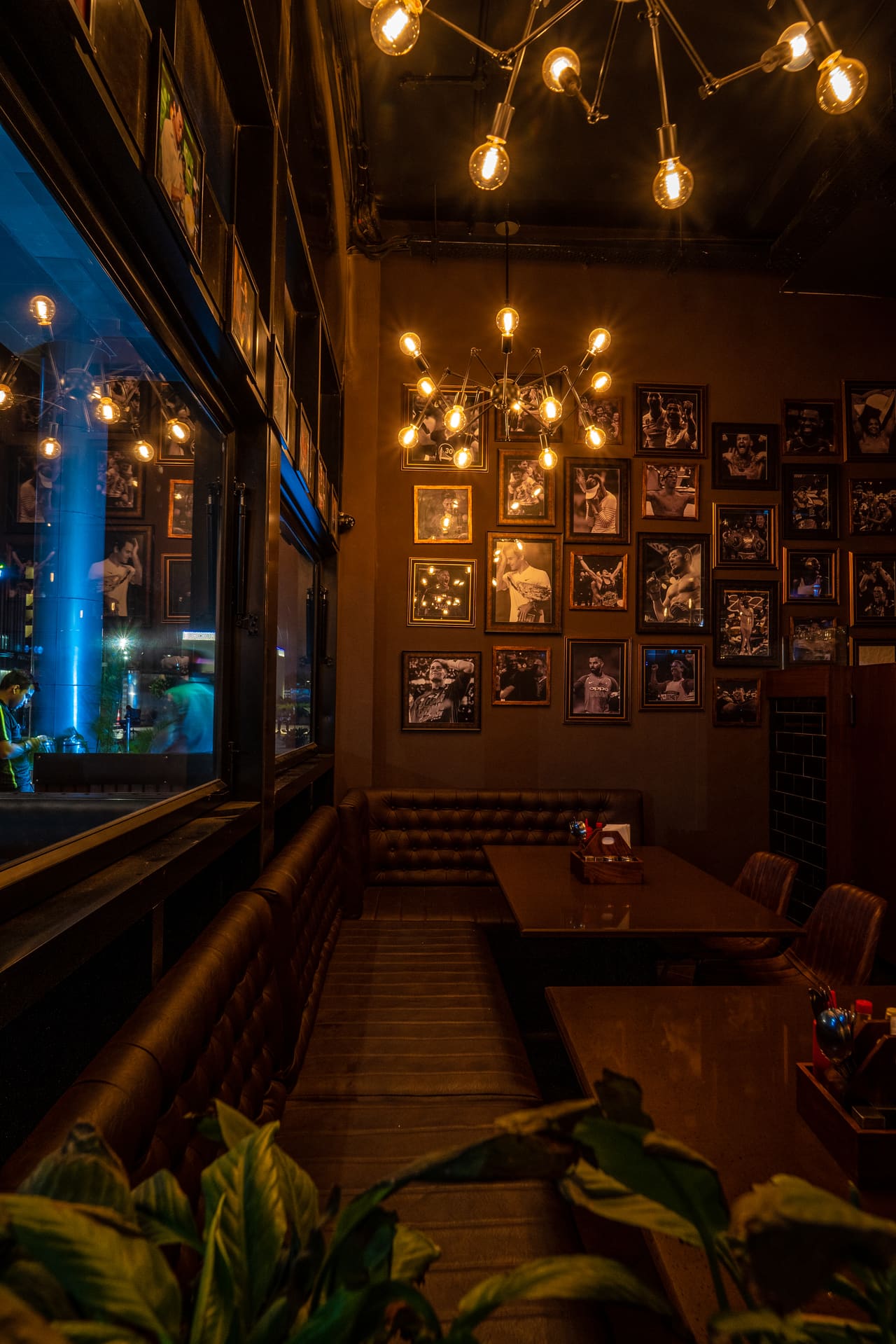 A narrow dining bay at Underdoggs Aerocity under a cluster of exposed-filament pendants, with framed photographs on the wall.