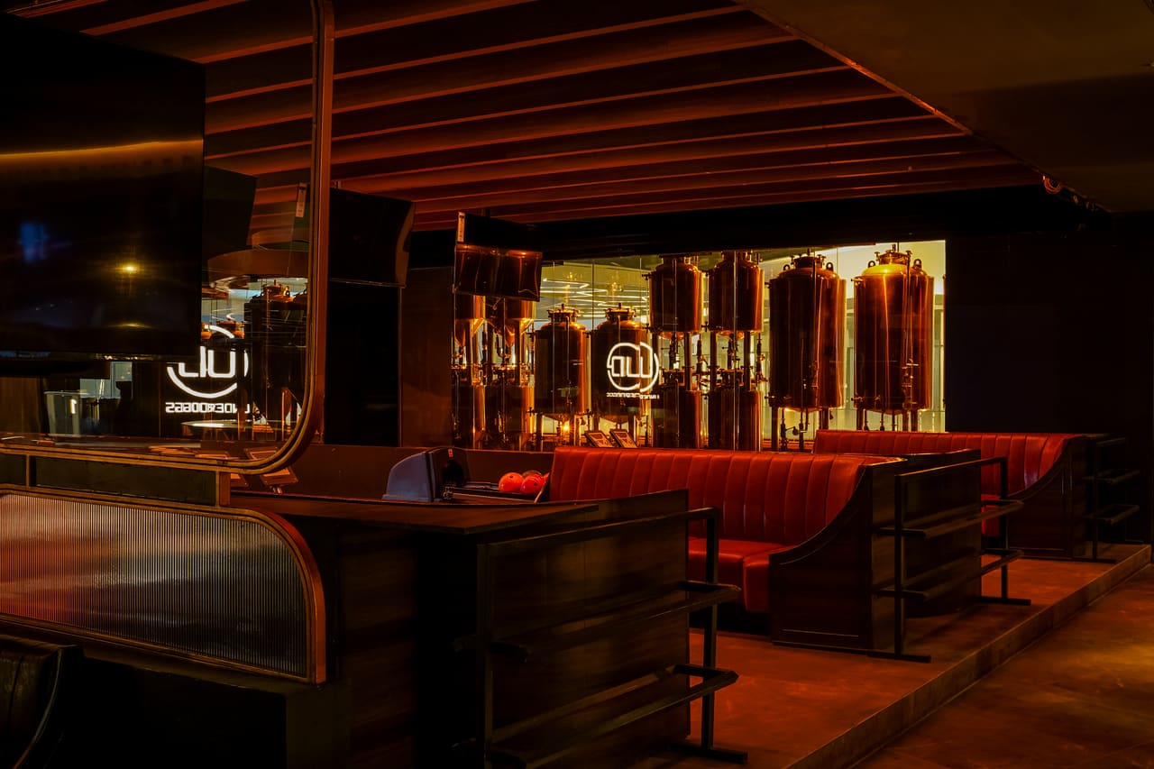 Copper brewing tanks behind glass at the back of a dim bar at Underdoggs Arena, with booths and the UD logo in the foreground.