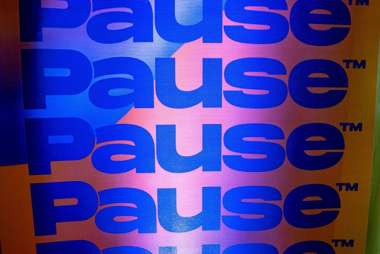 A wall printed with the word Pause, repeated in blue on pink and purple