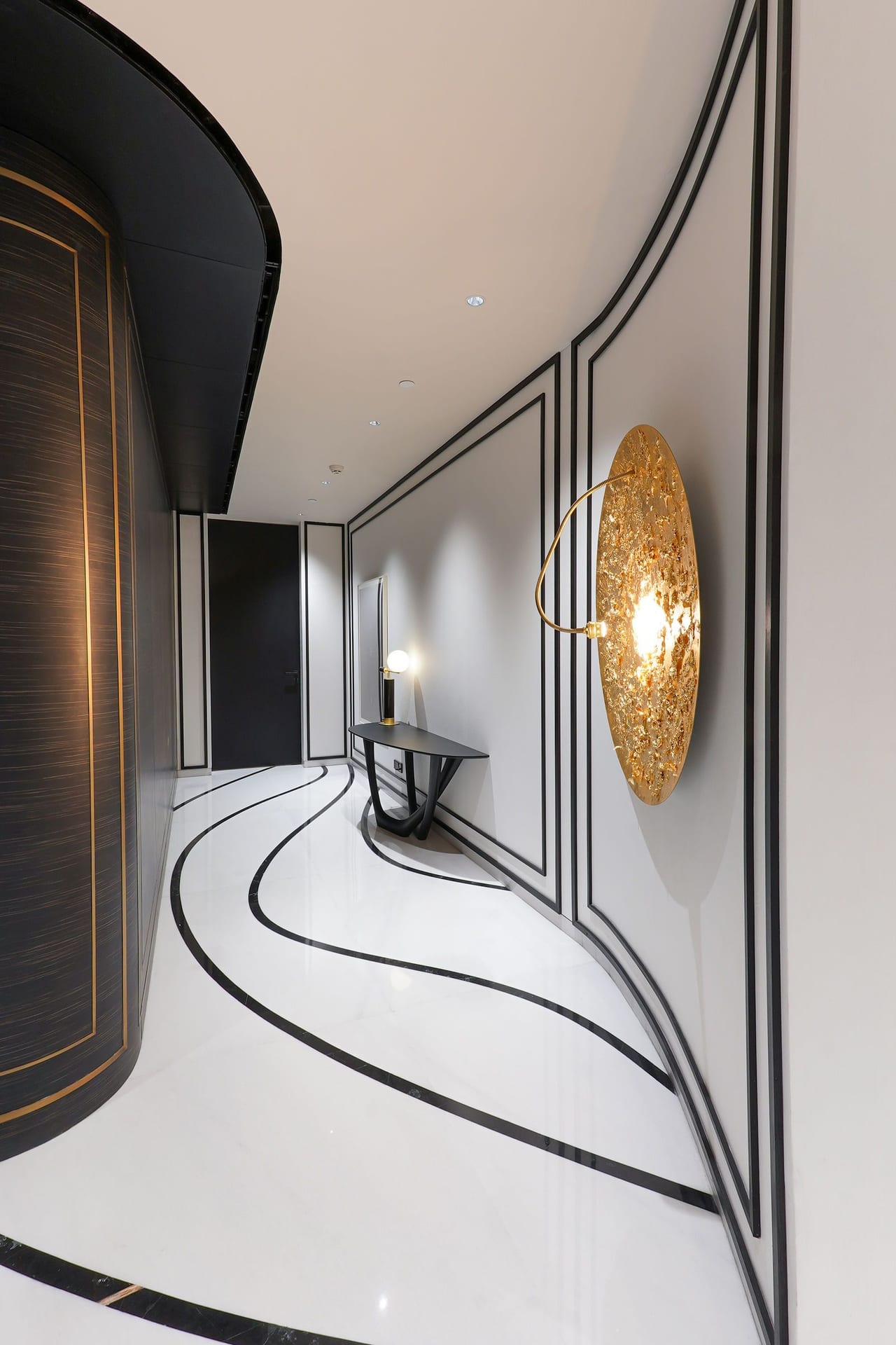A white corridor with curving black floor inlays leading to a gold wall disc