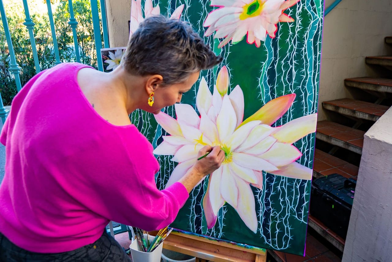 A woman in pink painting a large white flower on canvas