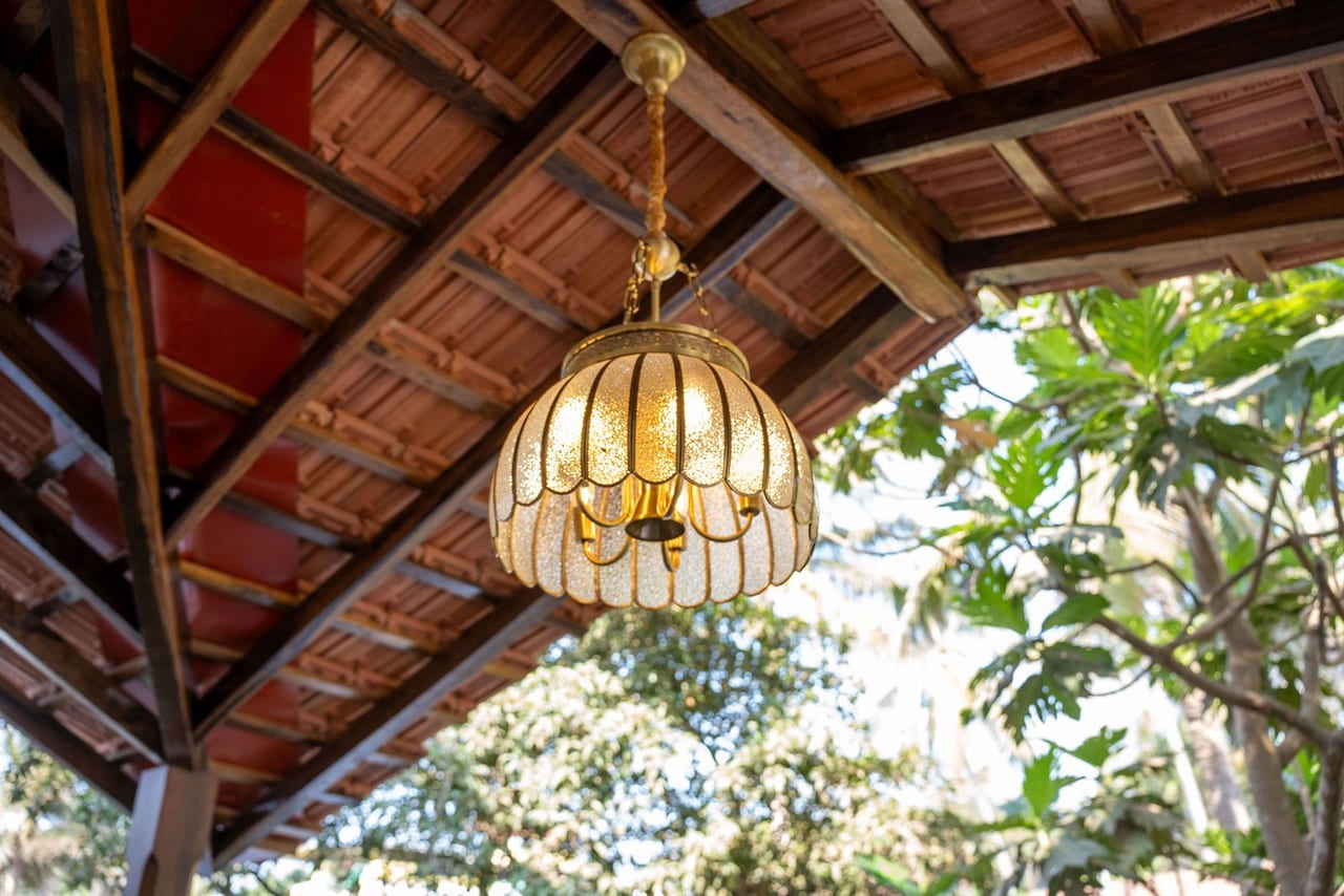 A woven pendant lamp hanging beneath a timber and terracotta roof