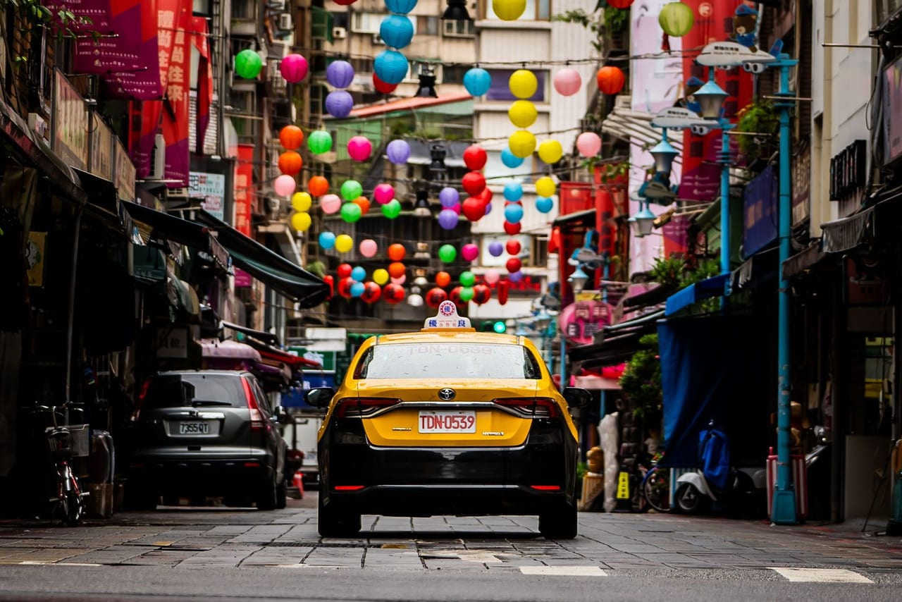 A yellow taxi on a street hung with colourful paper lanterns
