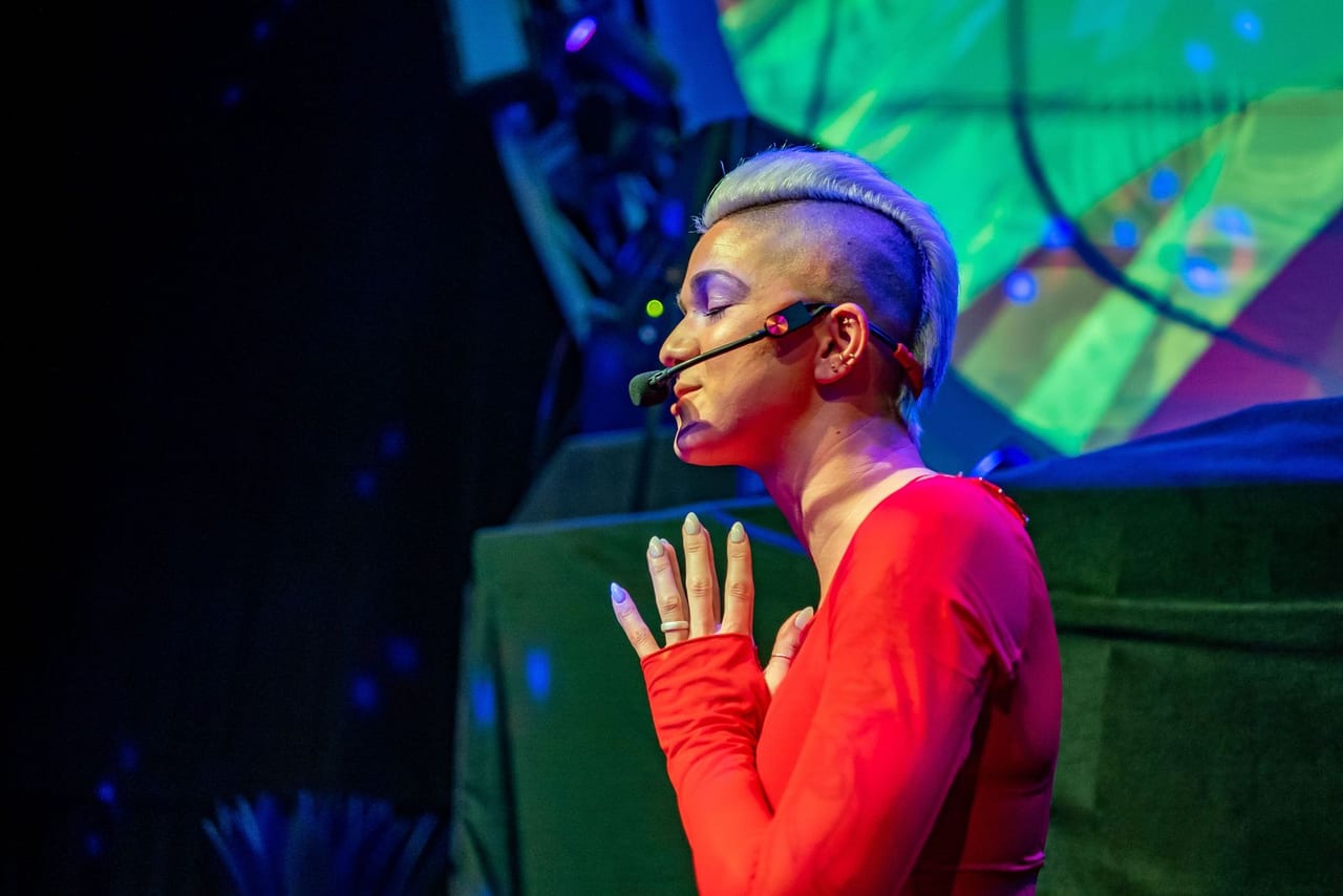 A yoga instructor in red speaking into a headset microphone in front of swirling projections